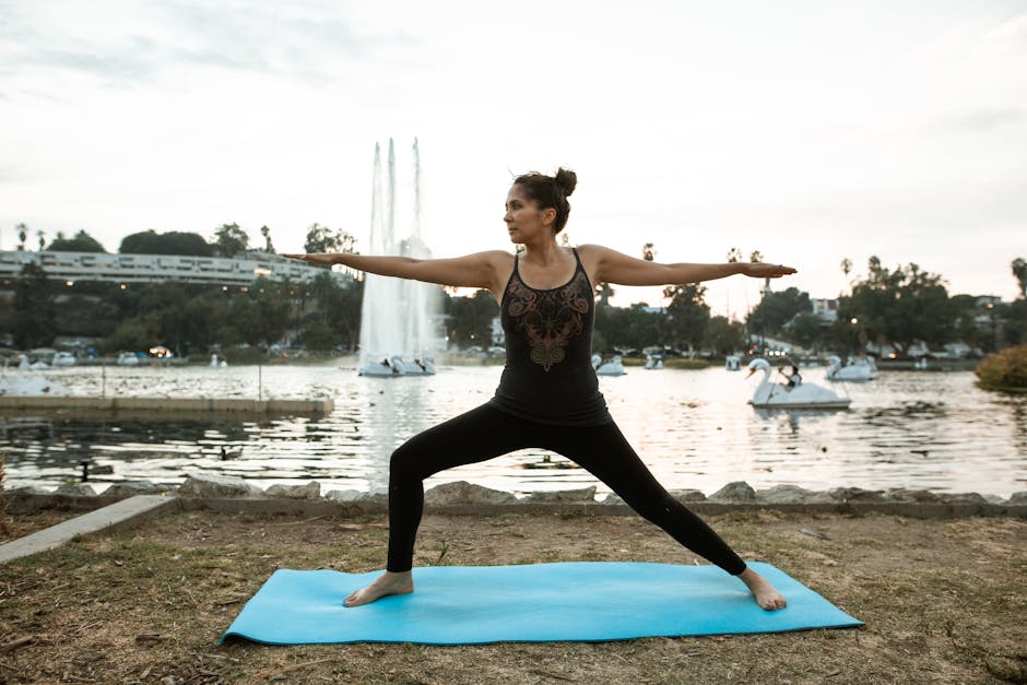 Person practicing yoga pose by the calm lake at sunset